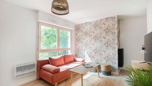 A cozy living room with a sofa, a coffee table, a woven rug, and a large window with a view of greenery.