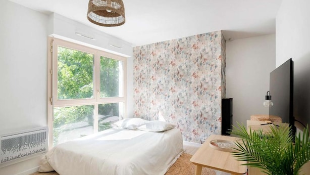 A bedroom with a bed, a desk, a TV, and a large window.