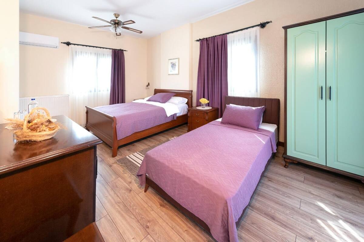 A hotel room with two beds, a wardrobe, a ceiling fan, and a window with purple curtains.