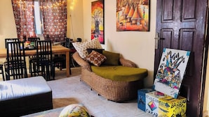 Een gezellige woonkamer met een rieten bank, een eettafel met stoelen en kunst aan de muren.