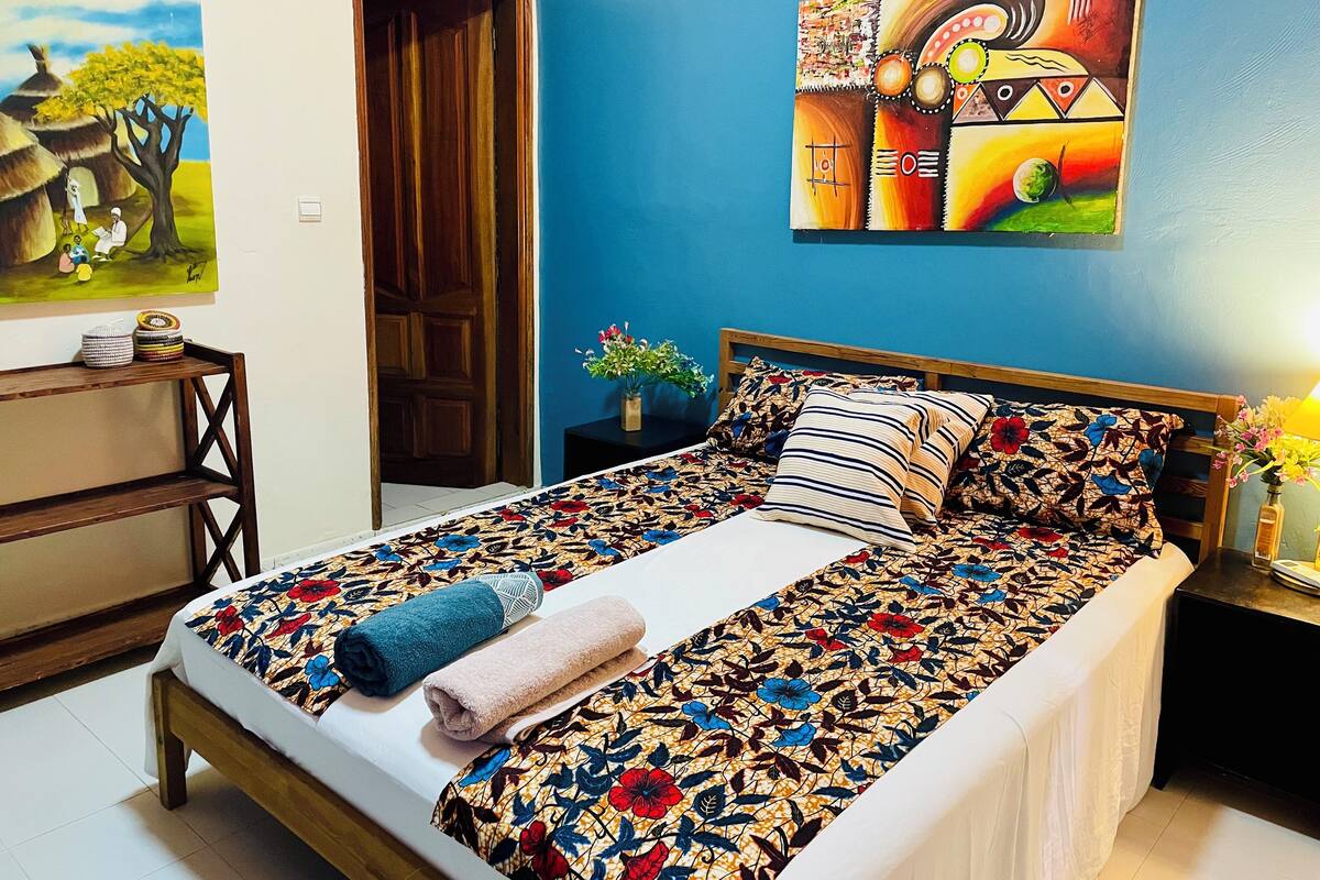 A bedroom with a bed, a nightstand, a painting, and a door.