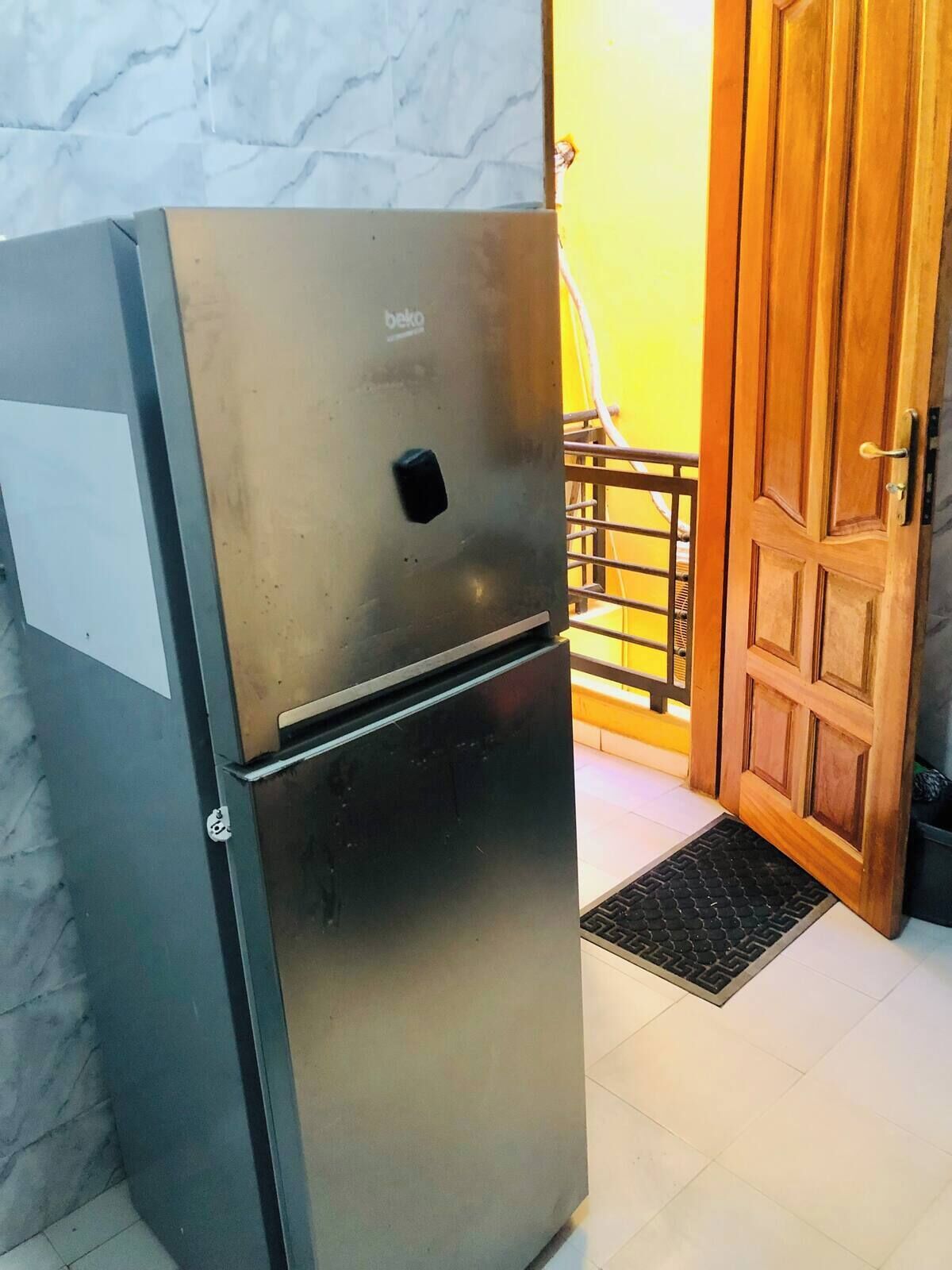 A stainless steel refrigerator in a room with a marble wall and a wooden door.