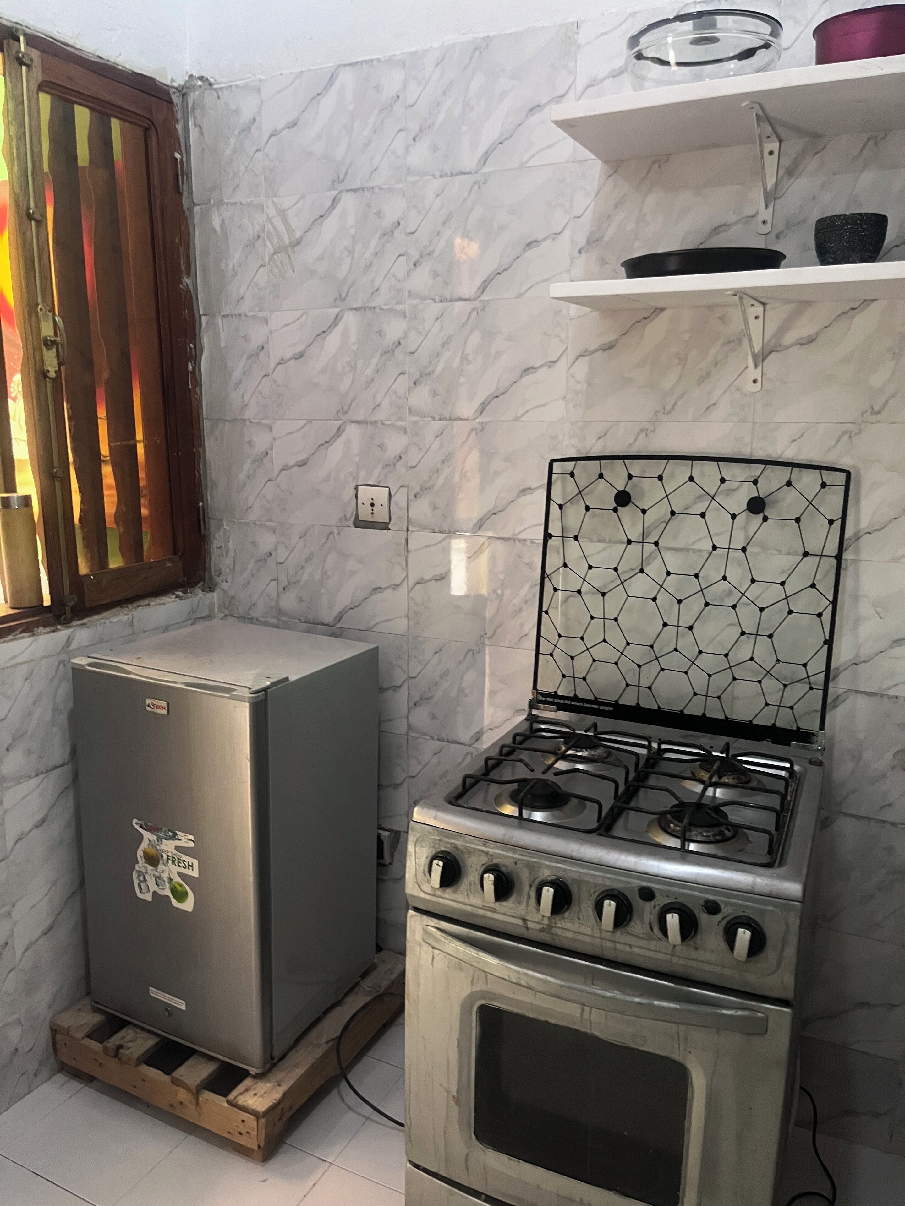 A kitchen with a gas stove, a refrigerator, and a window with vertical blinds.