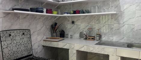 Una cocina con estufa a gas, repisas con vajilla y un salpicadero de mármol.