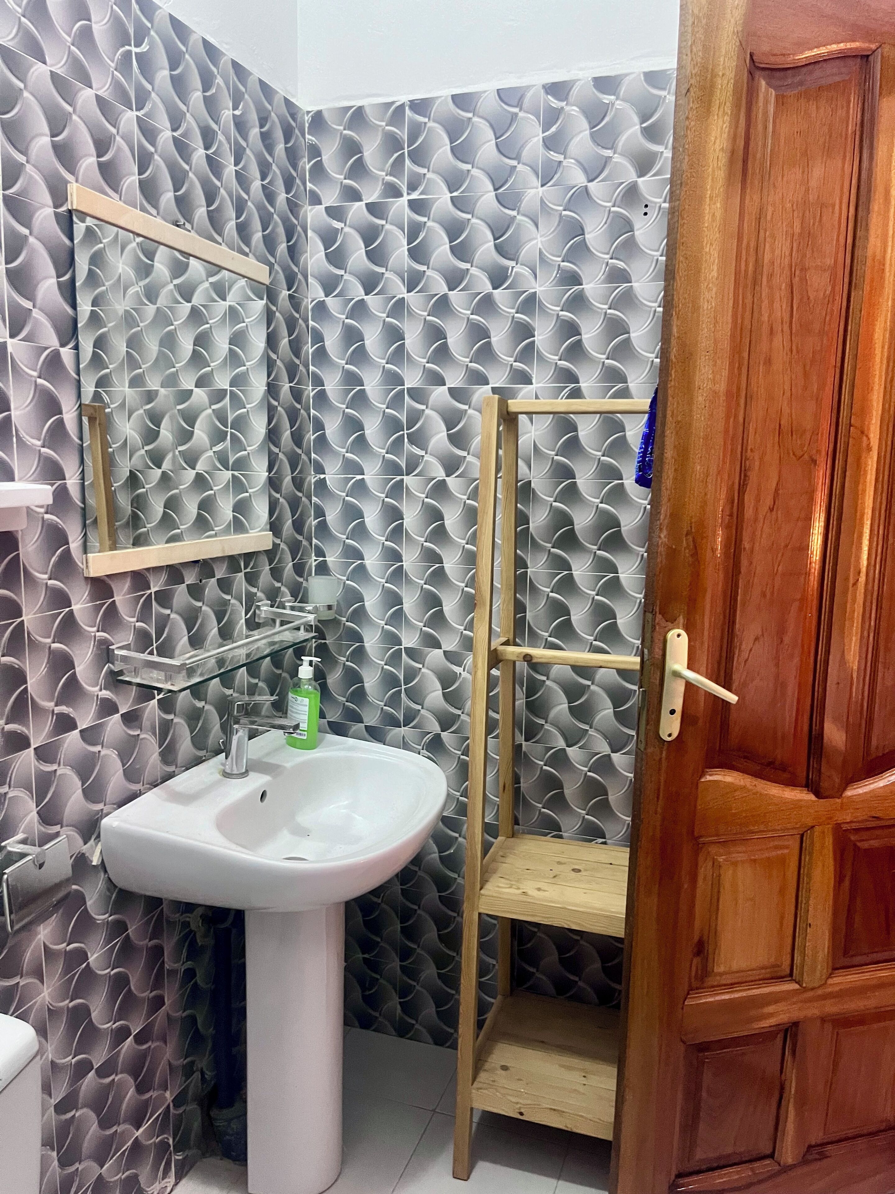 A bathroom with a white sink, a mirror, and a wooden shelf unit.