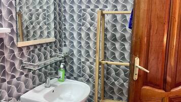 Un bagno con un lavandino bianco, uno specchio e una scaffalatura in legno.