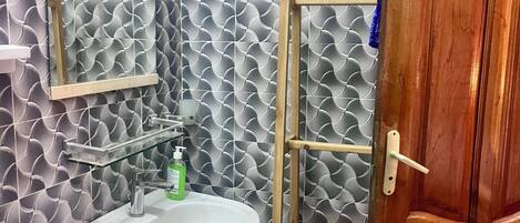 Un baño con lavamanos blanco, un espejo y una estantería de madera.