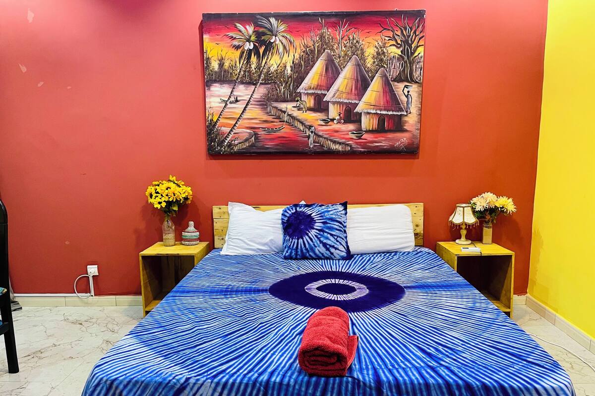 A hotel room with a bed, two nightstands, a painting on the wall, and a red towel on the bed.