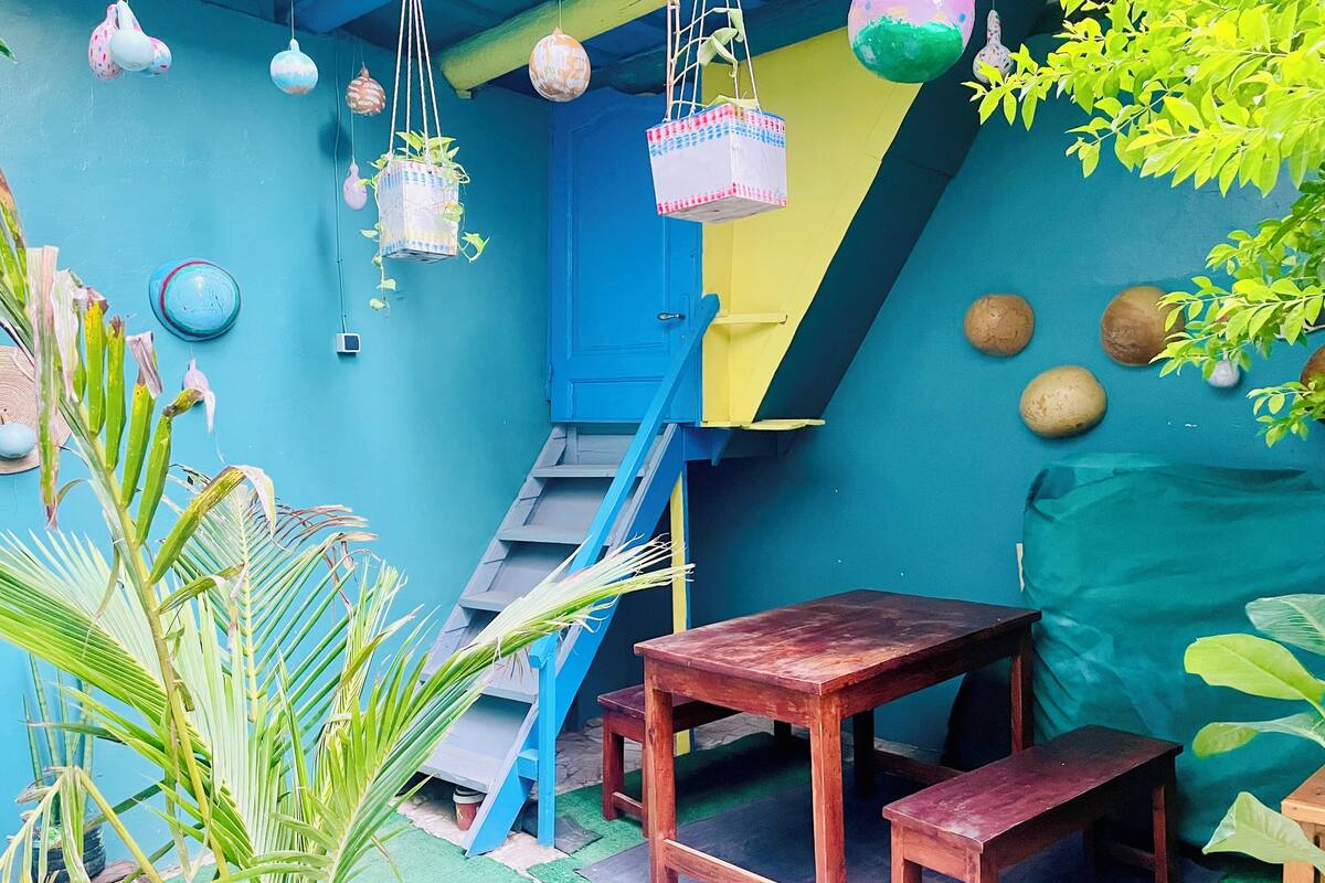 A room with a blue wall, a wooden table, a bench, a ladder, and hanging decorations.