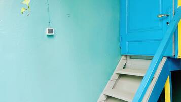 Un escalier surmonté d’une porte bleue, une plante suspendue et une petite balance.