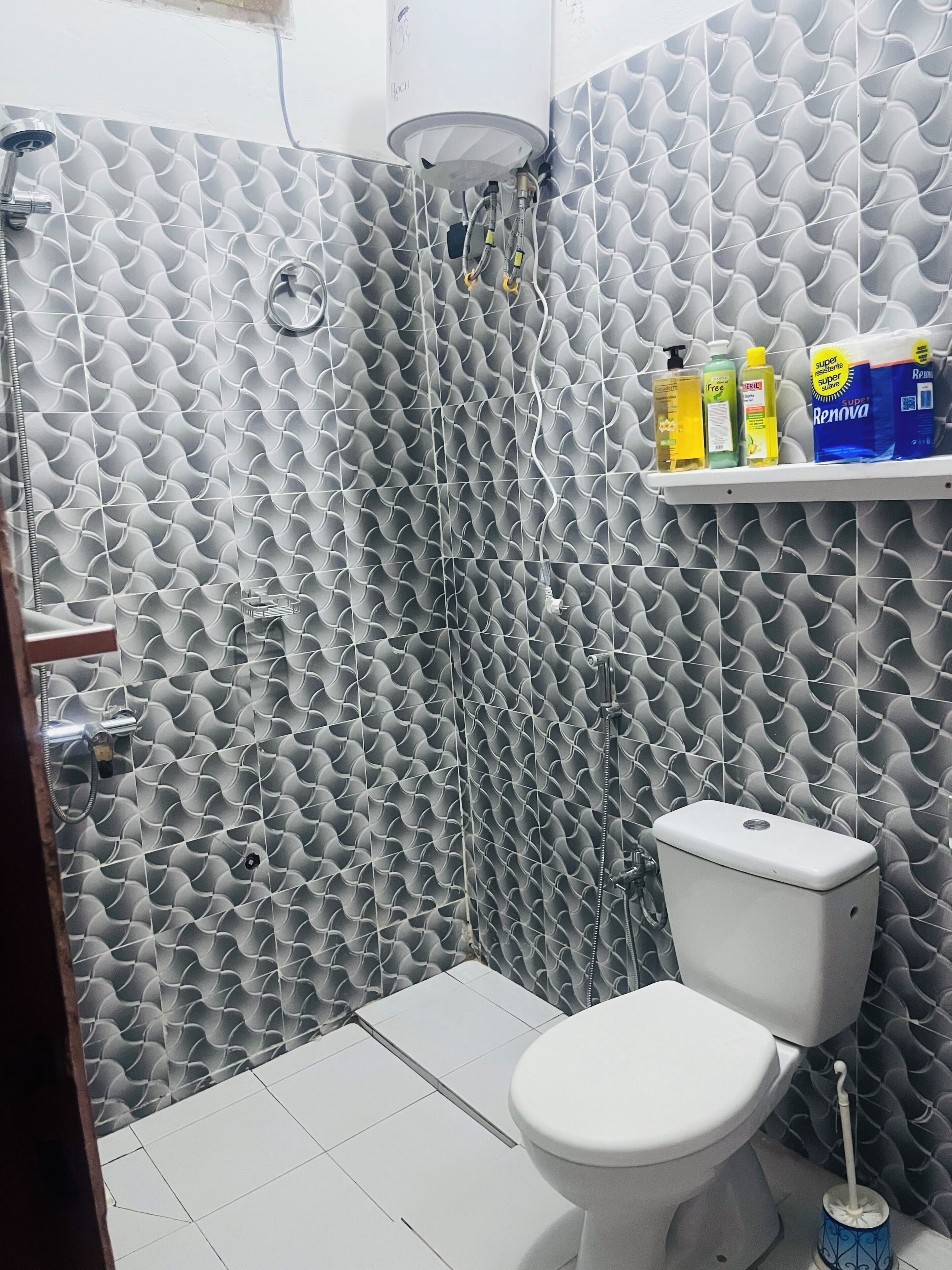 A bathroom with a patterned wall, a toilet, and a shelf with toiletries.
