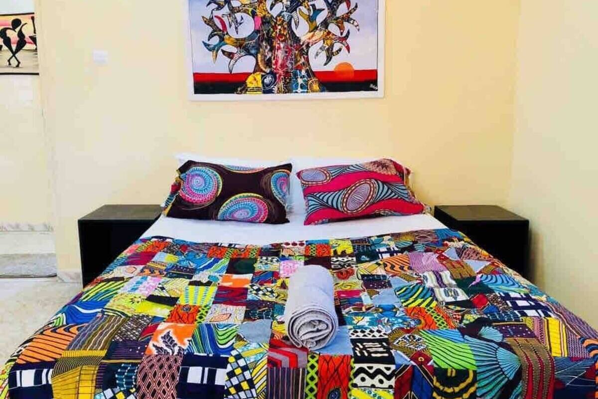 A bed with a colorful quilt, two pillows, and a painting on the wall.