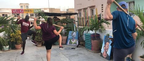 A courtyard with potted plants, a sign reading "VILLAGE FABIDI DIAM," and a mural on the wall.