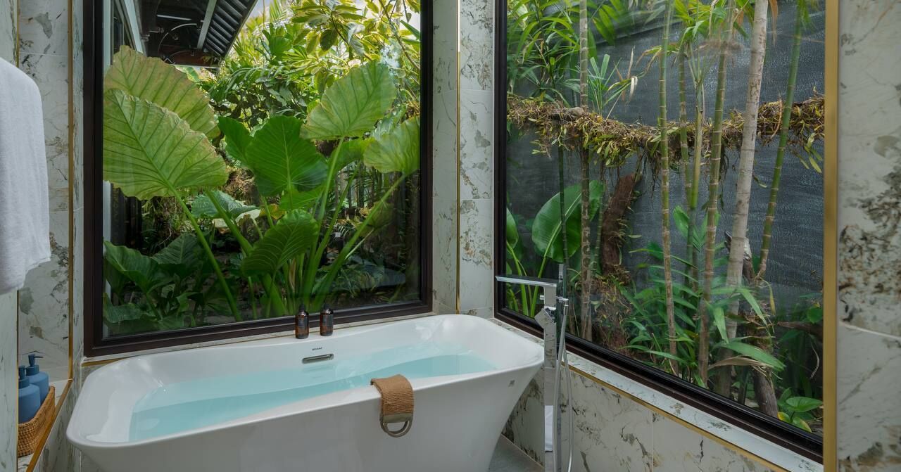 A bathroom with a bathtub, a window, and a view of a garden.
