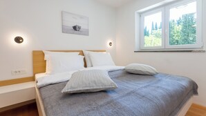 A neatly made bed with a gray bedspread and striped pillows, a wooden headboard, and a wall-mounted picture. - Premium Levant 212 Marina Apartment (Piran)