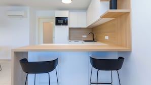 A modern kitchen with a central island, two black bar stools, a microwave, and a built-in oven. - Premium Levant 212 Marina Apartment (Piran)