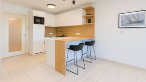 A modern kitchen with white cabinets, a wooden countertop, a black microwave, and a bar area with three black bar stools. - Premium Levant 212 Marina Apartment (Piran)