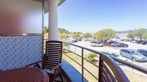 A balcony with a wooden chair and table, overlooking a parking lot and a clear blue sky. - Premium Levant 212 Marina Apartment (Piran)