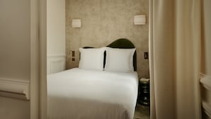 A hotel room with a large bed, beige walls, and two wall-mounted lights.