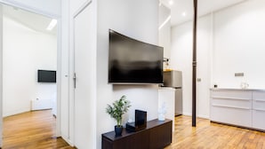 A modern living room with a large flat-screen TV mounted on the wall, a dark wooden console table with a plant, and a white cabinet with drawers. - Peaceful Apartment - 1br/4p - Eiffel Tower (Paris)