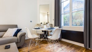 A modern living room with a grey sofa, a dining table with white chairs, and a large window with curtains. - Peaceful Apartment - 1br/4p - Eiffel Tower (Paris)