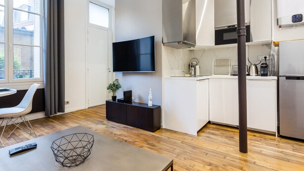 A modern living room with a flat-screen TV, a dining table, and a kitchen area with white cabinets and stainless steel appliances. - Peaceful Apartment - 1br/4p - Eiffel Tower (Paris)