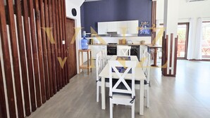 A modern kitchen with white cabinets, a blue wall, and a dining area with white chairs and a table. - Villa Nyota Eco Luxe (Jambiani)