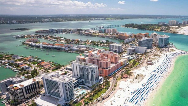 Vista aérea de una ciudad costera con un puerto deportivo, hoteles y una playa.