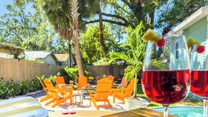 Un patio exterior con mobiliario de madera, una piscina y una copa de vino tinto.