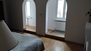 Une chambre à coucher avec un lit, un plancher en bois et deux fenêtres en arc de cercle.
