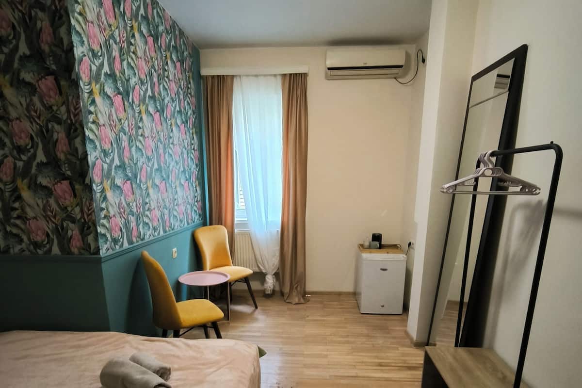 Una habitación de hotel con una cama, una silla, una mesita, un armario y un espejo.