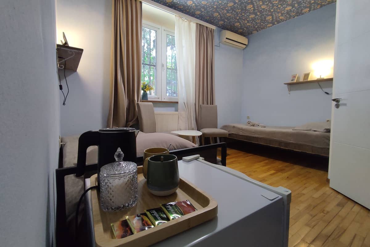 Una habitación acogedora con cama, una silla, una mesita con una bandeja de aperitivos, un radiador y una ventana con cortinas.