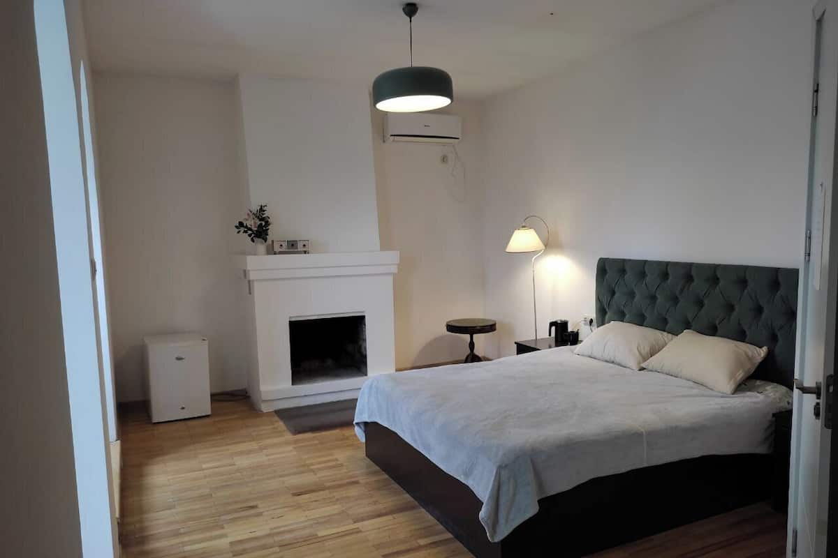 Un dormitorio con cama, chimenea, lámpara y una mesita.