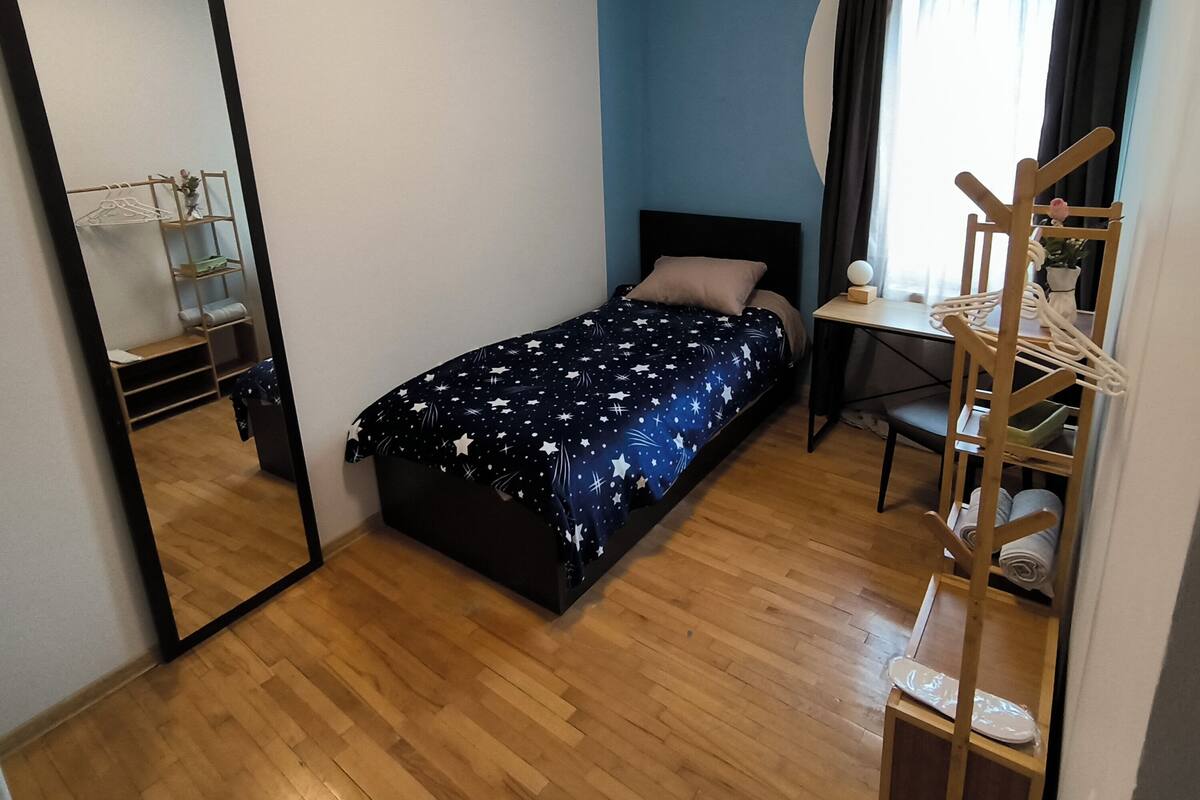 Un dormitorio con cama, escritorio, silla, espejo y aire acondicionado.