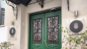 Une porte à deux battants, peinte en vert, ornée de motifs métalliques décoratifs, une enseigne indiquant l’hôtel Triple Eight, et un pot de fleurs placé à côté de l’entrée.