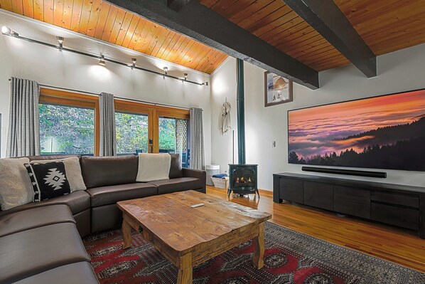 A modern living room with a sectional sofa, a wooden coffee table, a flat-screen TV, and a large window with curtains.