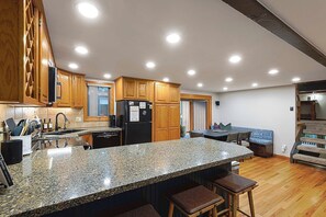 A kitchen with granite countertops, wooden cabinets, a black refrigerator, and a dining area with a bench and table.