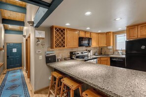 A kitchen with wooden cabinets, a granite countertop, a black refrigerator, and a microwave. - Alpine Adventure Lodge (Steamboat Springs)