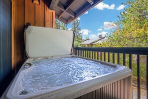 A hot tub with a wooden deck and a view of trees and a house in the background.