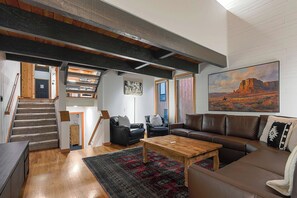A spacious living room with a staircase, a large painting, and a cozy seating area.