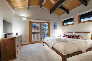 A bedroom with a bed, a dresser, a television, and a window with a view of a wooden structure outside.