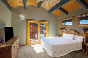 Un dormitorio con cama, televisor sobre una cómoda, ventilador de techo y puerta corrediza de vidrio que da a un espacio exterior.