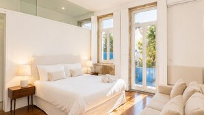 A bedroom with a large bed, a nightstand, a sofa, and a balcony with a view.