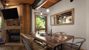A rustic dining area with a wooden table, leather chairs, a fireplace, and a television mounted on the wall.
