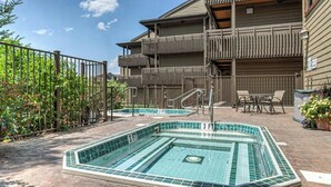 A pool area with a tiled deck, a pool, and a building with balconies.