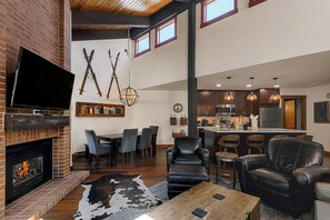 A modern living room with a fireplace, a dining area, and a kitchen with bar seating. - Alpine Retreat Lodge (Steamboat Springs)