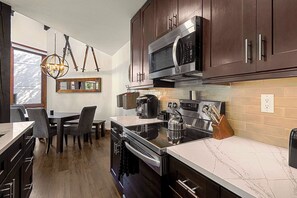 A modern kitchen with dark wooden cabinets, stainless steel appliances, and a marble countertop. - Alpine Retreat Lodge (Steamboat Springs)
