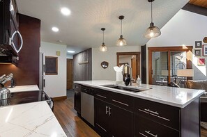 A modern kitchen with dark cabinetry, a marble countertop, and pendant lighting.