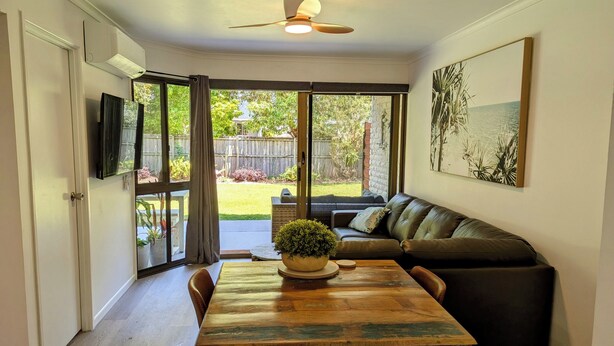 A dining area with a wooden table, chairs, a black leather sofa, and a ceiling fan.