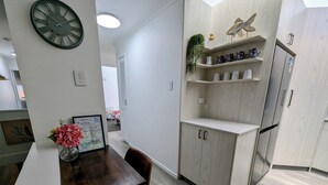 A modern kitchen with white cabinetry, a wooden dining table, and a clock on the wall.